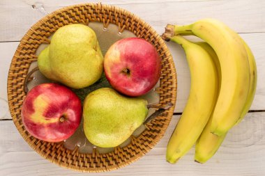 İki sulu organik armut, iki kırmızı elma ve ahşap bir masada seramik tabakla bir demet muz, yakın plan, üst manzara..