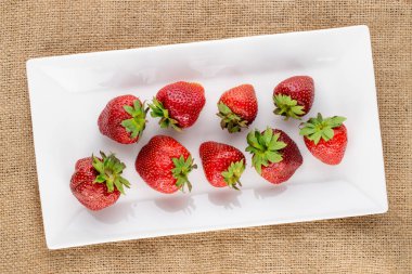 Beyaz seramik sofra takımlı olgun organik çilekler jüt kumaş, yakın plan, üst görünüm.