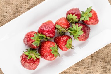 Beyaz seramik sofra takımlı olgun organik çilekler jüt kumaş, yakın plan, üst görünüm.