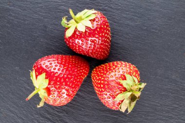 Üç meyve sulu tatlı çilek bir taş üzerinde, yakın plan, üst manzara.