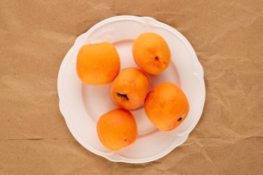 Beyaz seramik tabağı olan sulu kayısılar, el işi kağıt üzerinde, yakın plan, üst manzara..