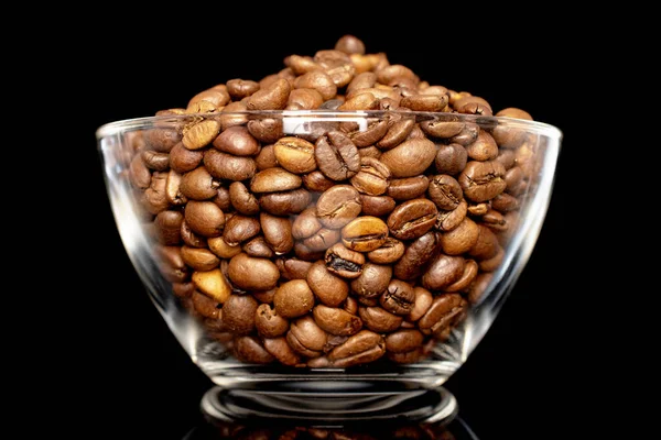 Roasted aromatic coffee beans in a glass bowl, close-up, isolated on a black background.