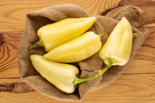 Tahta bir masanın üstünde, parlak sarı biberli, jüt çantalı, yakın planda, manzaralı birkaç biber..