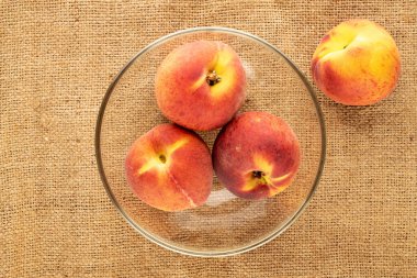 Jüt kumaş üzerinde cam bir tabakta birkaç sulu olgun şeftali, yakın plan, üst manzara.