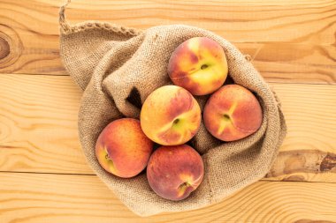 Tahta bir masada, yakın planda, üst görüntüde jüt torbasıyla sulu, olgun şeftaliler..