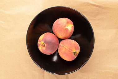 Üç sulu olgun şeftali siyah seramik bir tabakta kağıt üzerinde, yakın plan, üst görünüm.