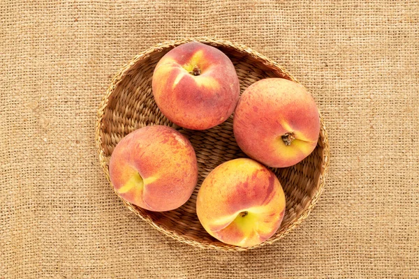 Pekçok sulu olgun şeftali, jüt kumaş üzerinde bir kamış plaka, yakın plan, üst manzara.
