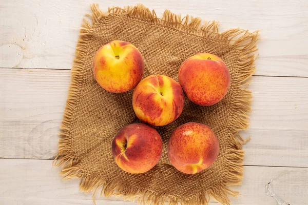 Tahta bir masanın üzerinde jüt peçeteyle sulu, olgun şeftaliler, yakın plan, üst manzara..