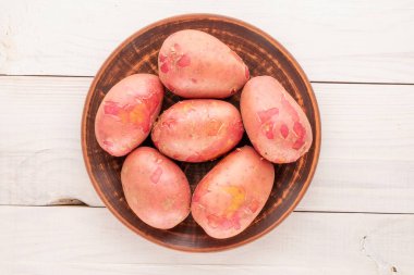 Tahta bir masanın üzerinde seramik tabakla birkaç organik pembe patates, yakın plan, üst manzara..