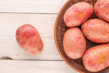 Tahta bir masanın üzerinde seramik tabakla birkaç organik pembe patates, yakın plan, üst manzara..