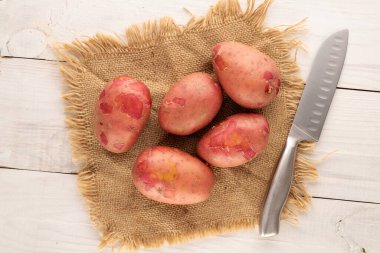 Bıçaklı birkaç organik pembe patates ve ahşap bir masa üzerinde jüt peçete. Yakın plan, üst görüş..