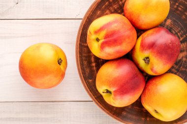 Tahta bir masanın üzerinde seramik bir tabakla, yakın plan, üst görünümü olan bir kaç olgun sulu nektarin..