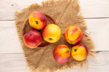 Tahta bir masanın üzerinde, yakın planda, üst görüntüde jüt peçetesi olan olgun, sulu nektarinler..