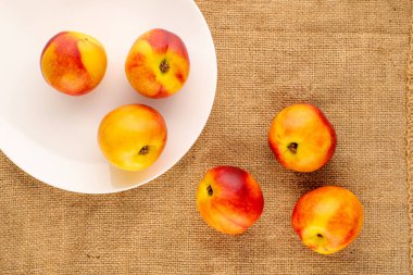 Jüt kumaşında beyaz seramik bir plaka ile birkaç olgun sulu nektarin, yakın plan, üst görünüm.