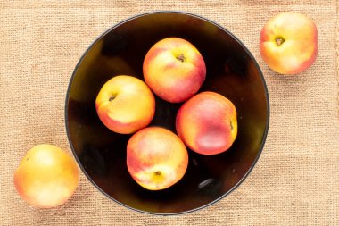 Jüt kumaşında siyah seramik bir plaka ile birkaç olgun sulu nektarin, yakın plan, üst görünüm.