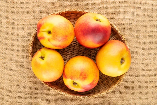 Birkaç olgun sulu nektarin, jüt kumaş üzerinde bir kamış plaka, yakın plan, üst görünüm.