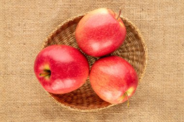 Üç sulu kırmızı elma jüt kumaş üzerinde bir kamış plaka, yakın çekim, üst manzara.