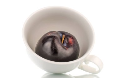 Beyaz seramik bardaklı, organik, koyu mor bir erik, yakın plan, beyaz üzerine izole edilmiş..