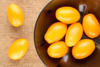 Birkaç olgun sarı domates, siyah seramik tabakta, jüt kumaş üzerinde, yakın plan, üst görüş..