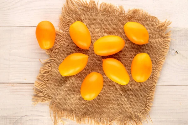 Several ripe yellow tomatoes with a jute napkin on a wooden table, close-up, top view.