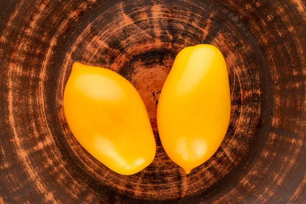 Two ripe yellow tomatoes on a clay dish, close-up, top view.
