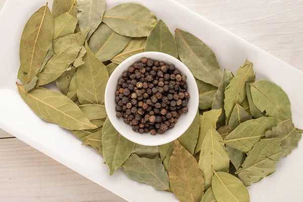 Kuru kokulu karabiber, defne yaprağı beyaz seramik kaplar ahşap bir masada, yakın plan, üst manzara.