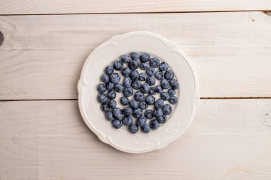 Beyaz bir tabakta organik yaban mersini, yakın plan, ahşap masa, üst görüş..