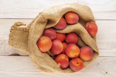 Ahşap bir masanın üstünde, üst tarafta, jüt bir çantada birkaç organik kırmızı kayısı var..