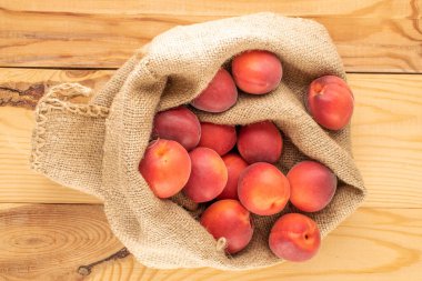 Ahşap bir masanın üstünde, üst tarafta, jüt bir çantada birkaç organik kırmızı kayısı var..