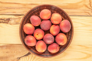 Ahşap bir masada, yakın planda, üstten görünüşlü, kilden bir tabakla birkaç tatlı kırmızı kayısı..