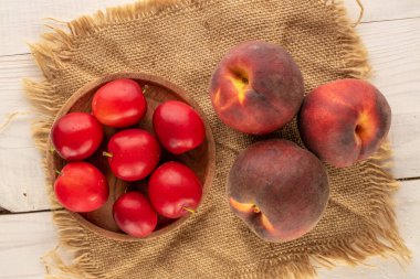 Birkaç tatlı vişneli erik ve üç şeftali. Tahta bir masanın üstünde jüt peçetesi, yakın plan, üst manzara..