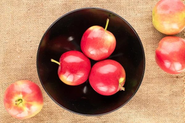 Several juicy red apples with a black ceramic plate on a burlap, macro, top view.