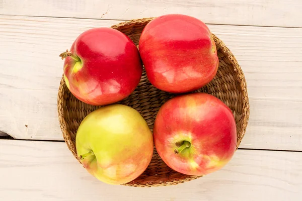 Four juicy red apples with a straw plate on a wooden table, macro, top view.