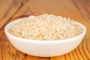 Organic uncooked rice in a white ceramic saucer on a wooden table, close-up.