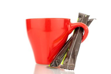 Two sticks of sugar in a paper bag with a red ceramic cup, close-up, isolated on a white background.