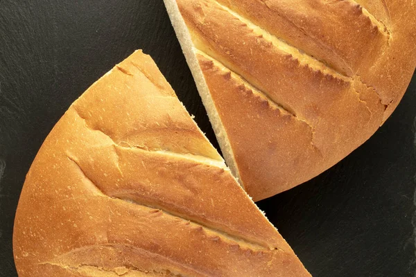 Two halves of a fragrant fresh long loaf on a slate stone, close-up, top view.