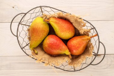 Four juicy pears in a basket on a wooden table, close-up, top view.
