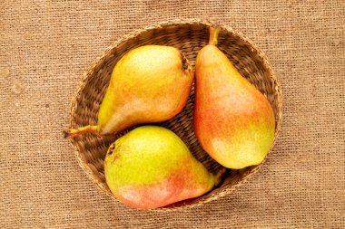 Three sweet ripe pears with a straw plate on a jute cloth, close-up, top view.