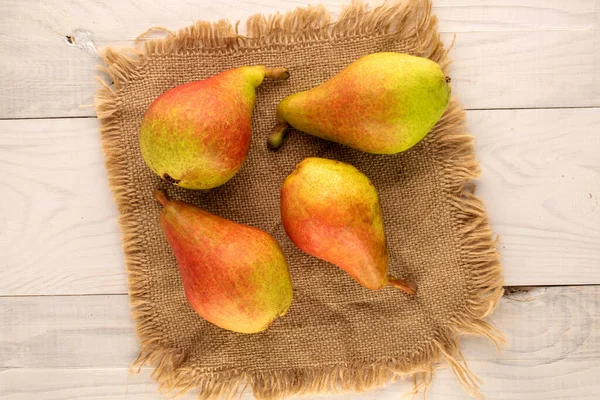 Four juicy pears with a jute napkin on a wooden table, close-up, top view.