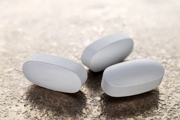 Three vitamin tablets on a metal platter, close-up.