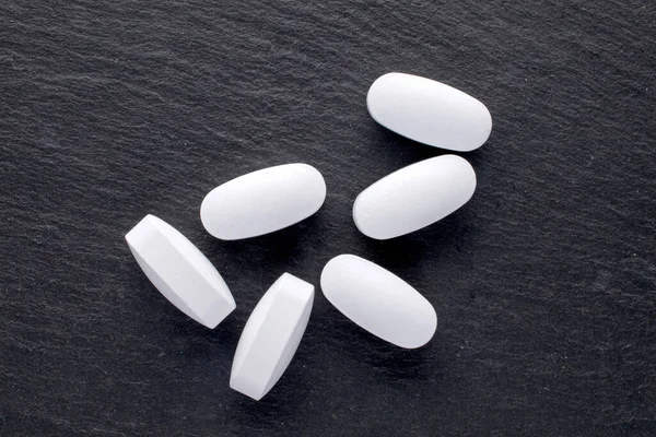 Several vitamin tablets, close-up, on a slate stone, top view.