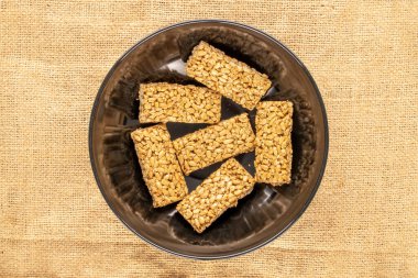 Several sweet candies Grillage from sunflower seeds and honey in a black ceramic dish on burlap, macro, top view.