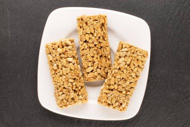 Three sweet candies Grillage from sunflower seeds and honey with a white ceramic saucer on a slate stone, macro, top view.