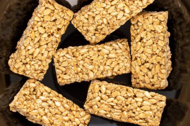 Several sweet candies Grillage from sunflower seeds and honey on a black ceramic dish, macro, top view.