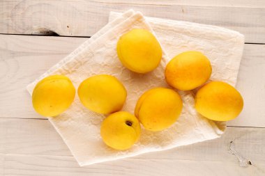 Several bright yellow juicy pineapple apricots with a white linen napkin on a wooden table, macro, top view.