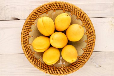Several bright yellow juicy pineapple apricots in a ceramic plate on a wooden table, macro, top view.