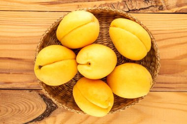 Several bright yellow juicy pineapple apricots with a straw plate on a wooden table, macro, top view.