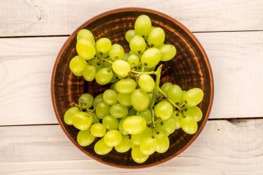 One bunch of white grapes with a ceramic plate on a wooden table, close-up, top view.