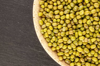 Several grains of organic uncooked mung beans with a  ceramic saucer on a slate stone, close-up, top view.