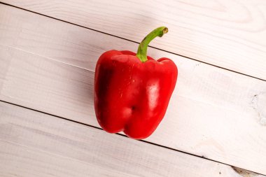 One whole organic fresh juicy delicious bell pepper, close-up, on a painted white tabletop made of wood, top view.